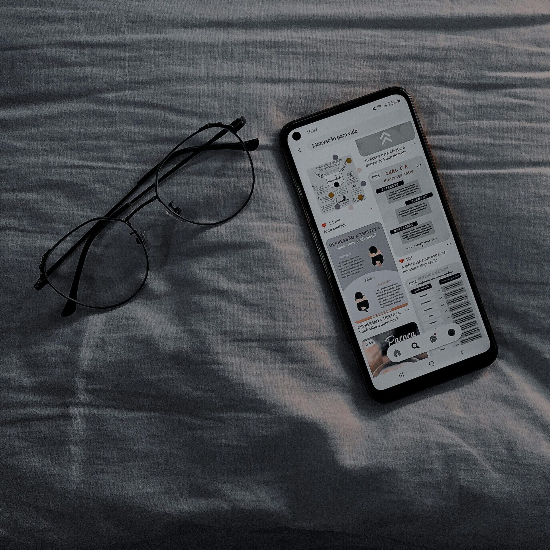 A smartphone and eyeglasses resting on a bedspread, creating a casual still life scene.